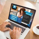 a senior man looking at senior living communities on his laptop with a cup of coffee on his desk